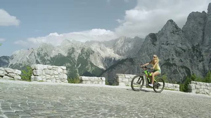 慢动作: 开朗的女孩在夏天轻松地在山口上骑电动自行车