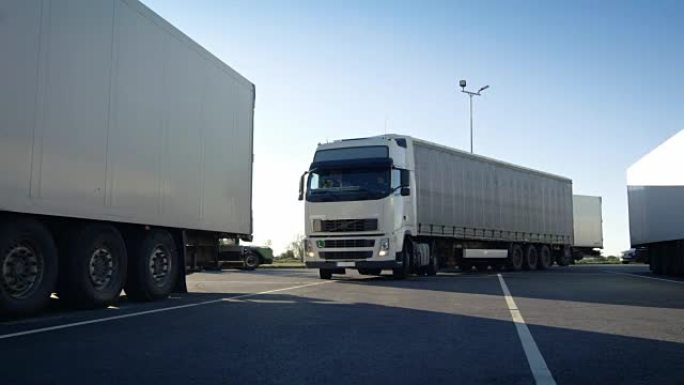 带有货运拖车的白色半卡车驶入停车场，并与其他车辆一起停放。