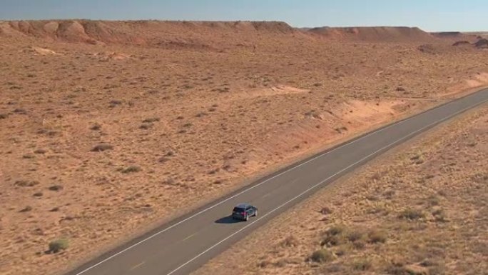 空中: 黑色SUV吉普车沿着直空的道路驶过干燥的沙漠