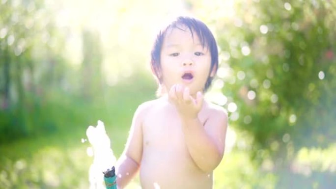 可爱的亚洲男婴在院子里玩水时露齿的微笑。