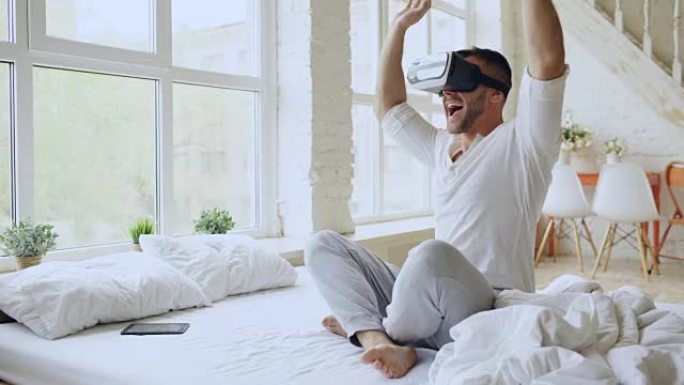 年轻开朗的男人戴着虚拟现实耳机，坐在家里的床上有360的VR视频体验