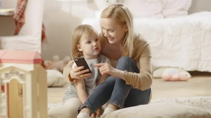 美丽的母亲和她的小女儿聊得很开心，母亲拿着智能手机。儿童房里摆满了玩具。
