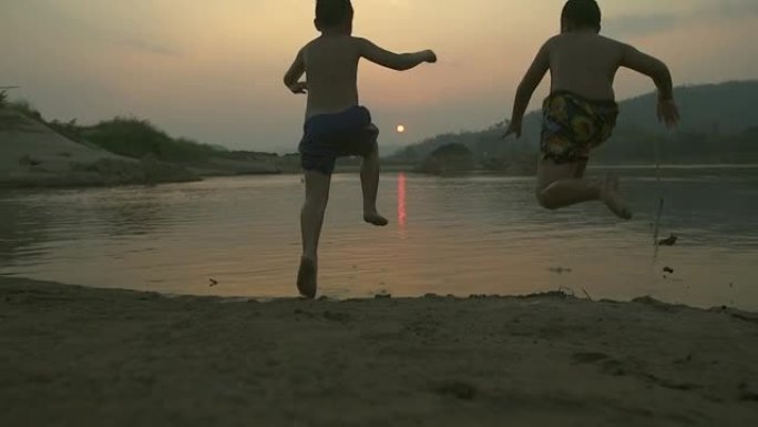 剪影快乐的孩子在日落时在池塘里嬉戏。(慢动作)