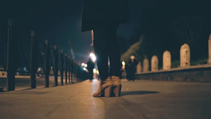 女性腿穿高跟鞋的特写镜头。女人晚上站在桥上等待