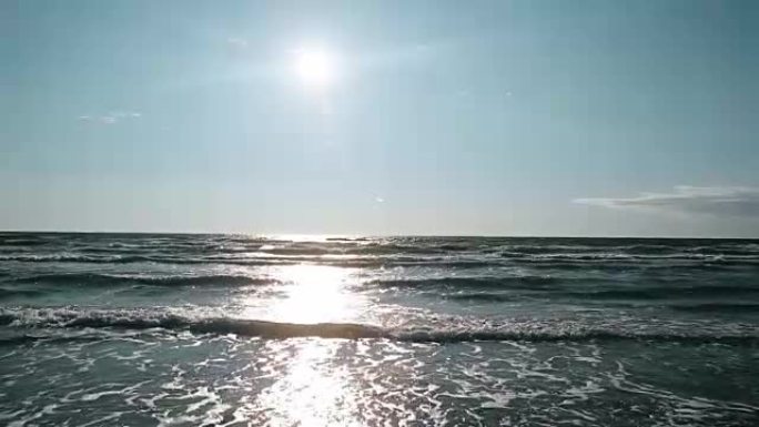 蓝天中明亮的太阳照在海面上，海浪在灯光中闪闪发光