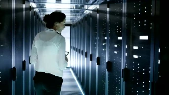 女性服务器技术人员带着成排的机架服务器走在数据中心走廊上。她在平板电脑上运行诊断程序