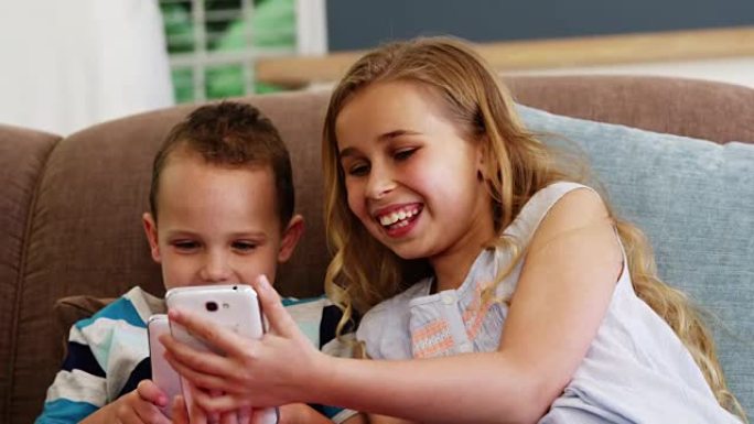 微笑的男孩和女孩坐在沙发上使用手机