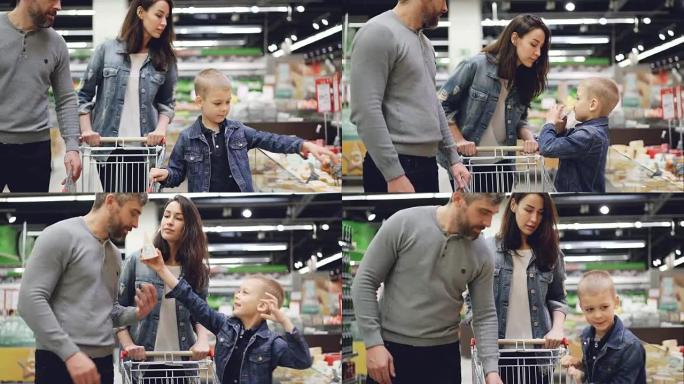小男孩正在和他的父母一起购物，从冰箱里拿奶酪闻起来，然后送给父母，他们正在检查产品质量并放入购物车。