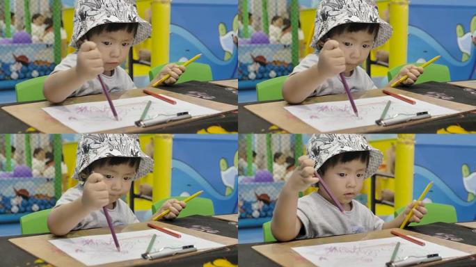 一个男孩 (12-23个月) 在客厅的桌子上选择铅笔并做作业