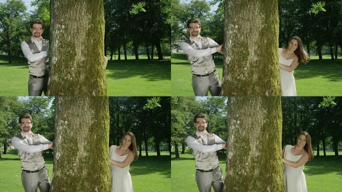 慢动作恋爱中的年轻夫妇从阳光明媚的绿色公园的一棵大树后面偷看