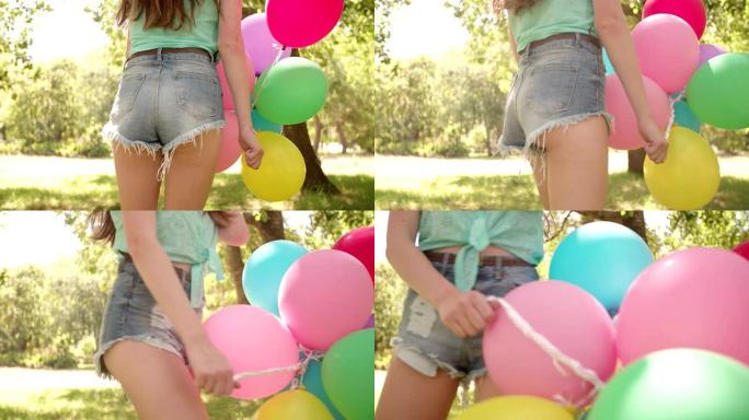 阳光明媚的公园里带着五颜六色气球的快乐女孩
