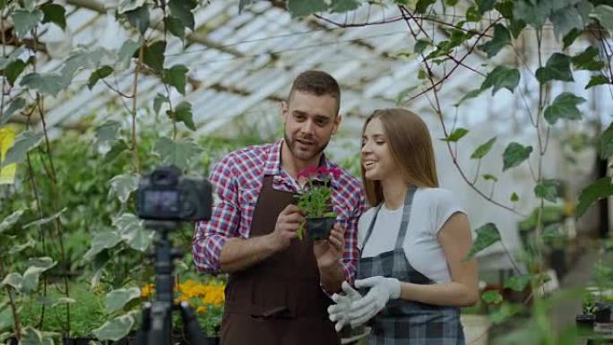 年轻微笑的博主夫妇园丁围着围裙，拿着花说话，录制在线园艺视频博客