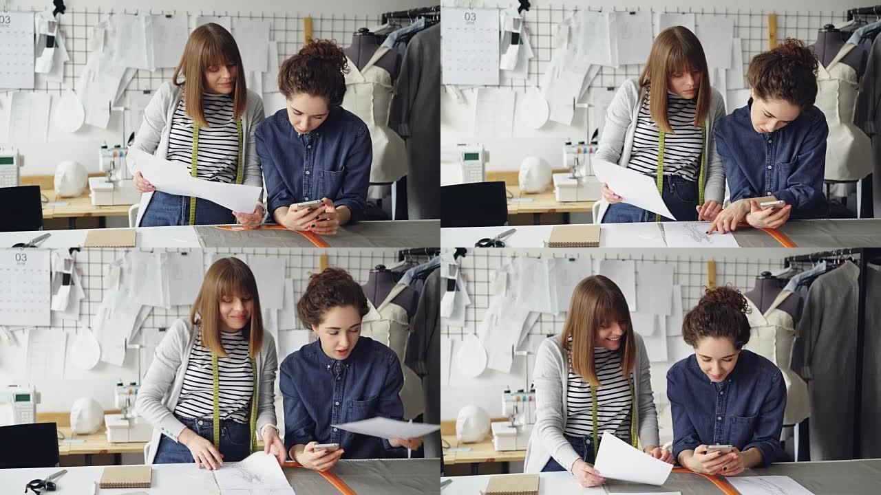 年轻的服装设计企业家正在研究草图并检查智能手机。有魅力的女人正在友好地讨论时装业。