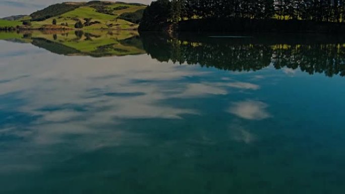 鸟瞰图飞越湖面，驶向新西兰绿草如茵的山丘。镜面反射