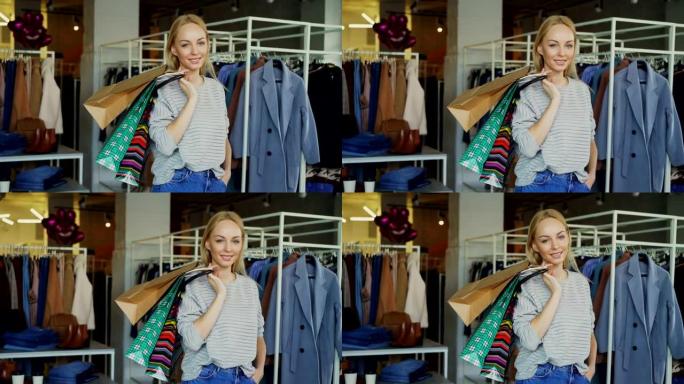 迷人的年轻女子的肖像站在服装店里，拿着许多纸袋，开心地微笑着看着相机。时髦的衣服是背景。