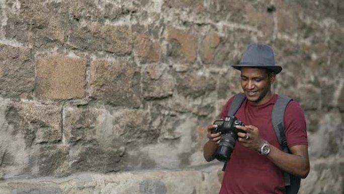 非裔美国快乐游客在他的单反相机上拍照。站在欧洲著名建筑附近的年轻人