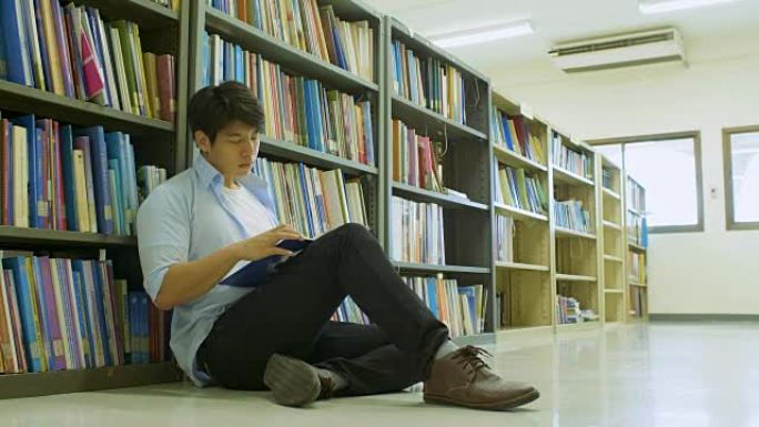 男大学生坐在图书馆的地板上看书