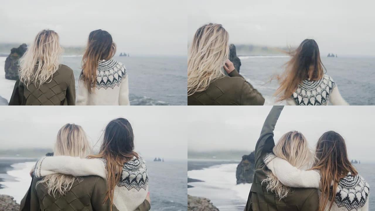 两个快乐的女人一起旅行。女孩在冰岛巨魔脚趾附近的海滩上玩得开心，举起双手拥抱