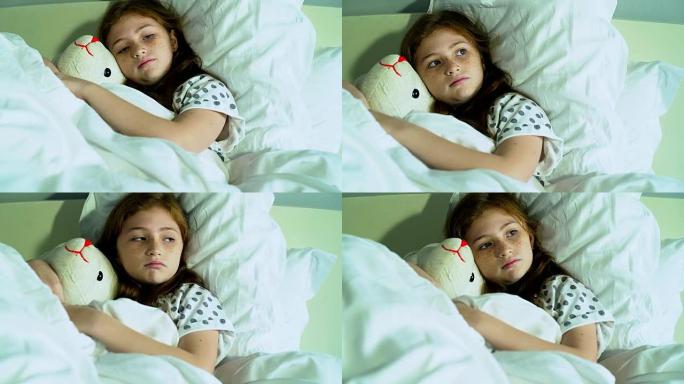 可爱的小女孩带着她的泰迪熊，躺在床上，家里带着悲伤的喜怒无常