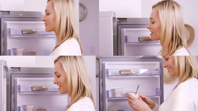 金发女人在冰箱上吃酸奶