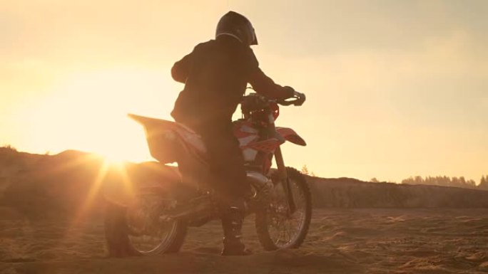 专业的FMX摩托车骑手旋转全油门手柄，开始在沙地越野赛道上骑行。风景优美的日落。