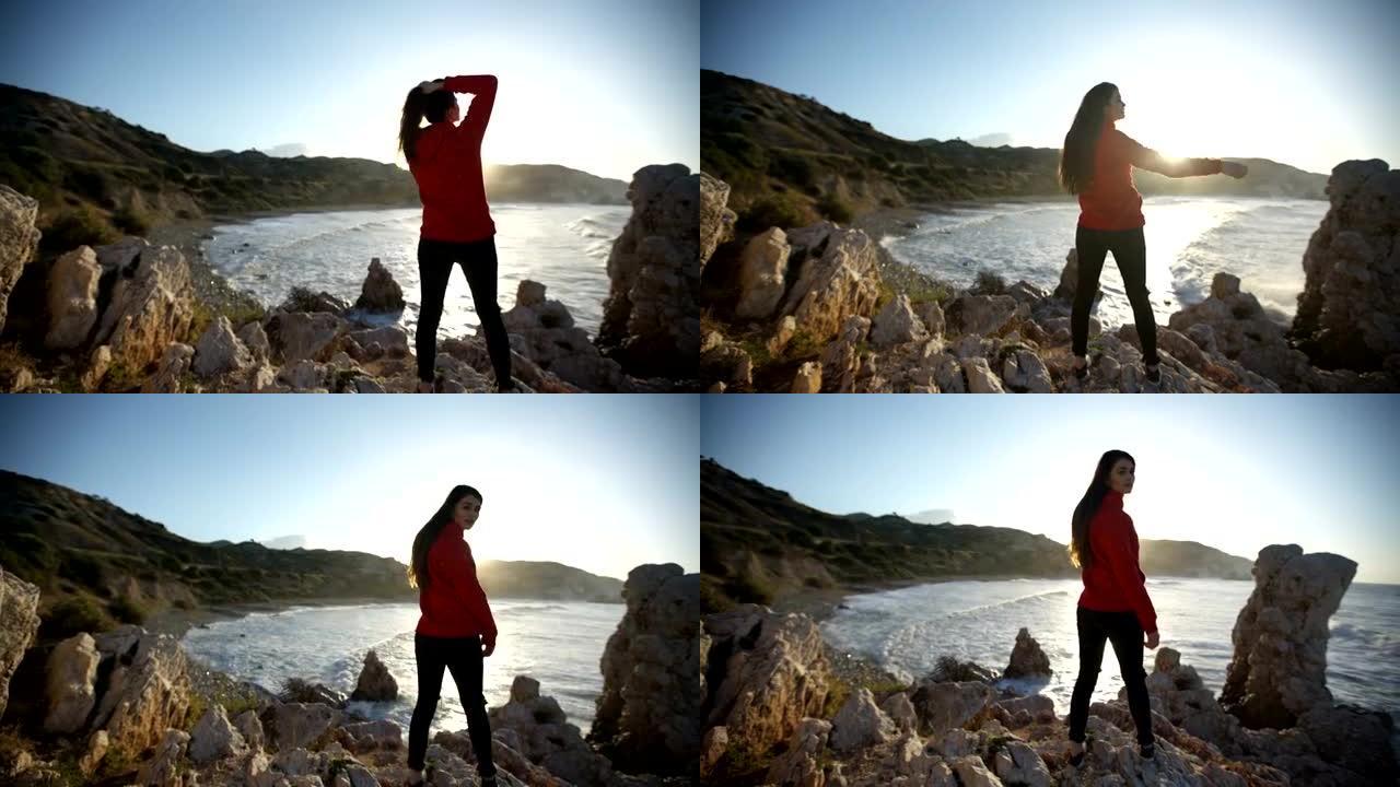 年轻女子在岩石海岸线上摆姿势。日落