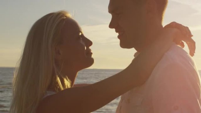 女孩和男人互相拥抱，在日落的沙滩上接吻