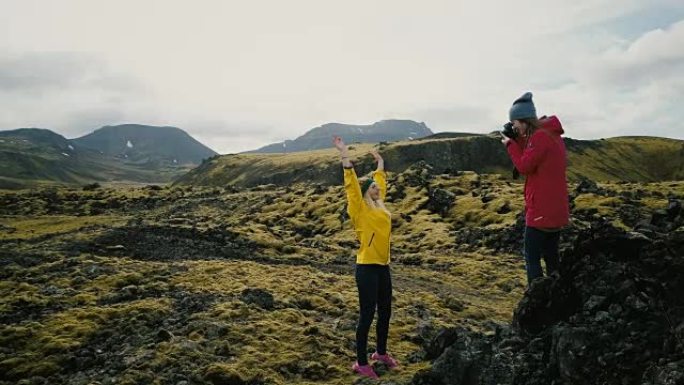 摄影师在山里给旅游女人拍照。在冰岛的熔岩田里拍照的女孩