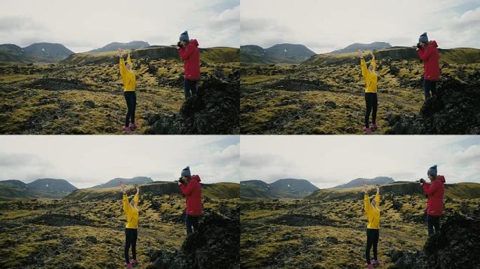 摄影师在山里给旅游女人拍照。在冰岛的熔岩田里拍照的女孩
