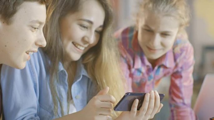 在学校科学课项目中工作的男孩和两个女孩在智能手机上观看受欢迎的视频。
