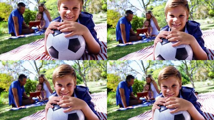 微笑的男孩在4k公园野餐时靠在足球上