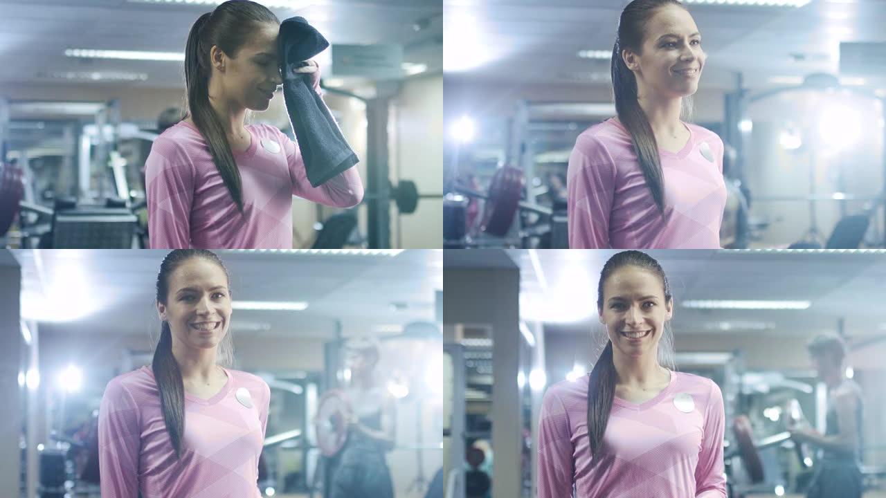 迷人的运动女孩正在用毛巾擦脸，在健身房摆姿势。