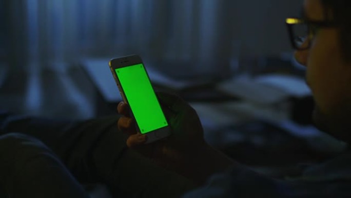 男人晚上躺在沙发上，在肖像模式下使用绿屏手机。