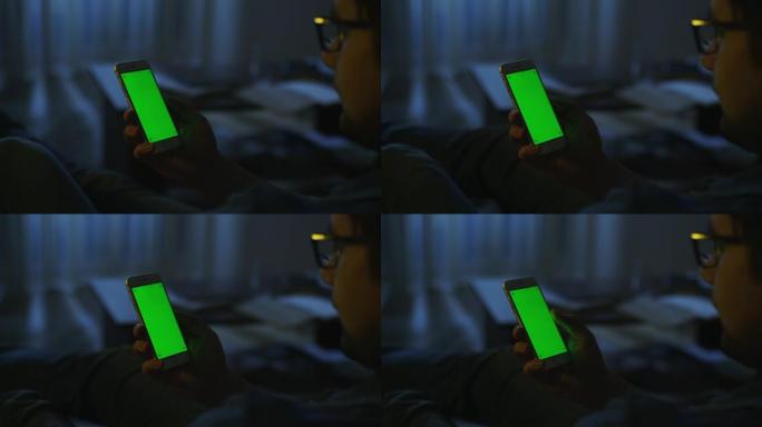男人晚上躺在沙发上，在肖像模式下使用绿屏手机。