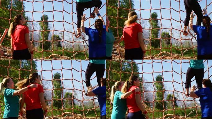 女教练在障碍赛中协助妇女攀爬网