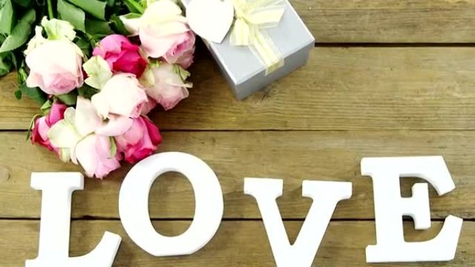木板上有一束玫瑰和爱情字母的礼品盒