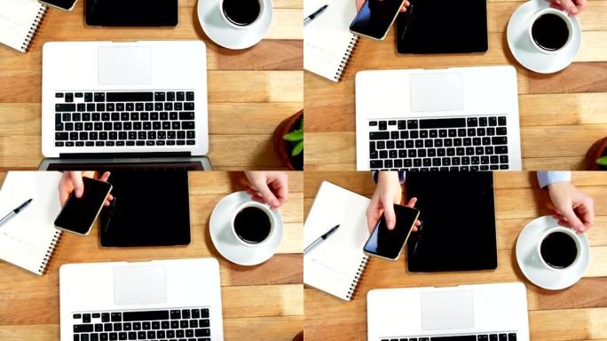 女商人的手在桌子上使用手机，桌上放着咖啡，笔记本电脑和数字平板电脑