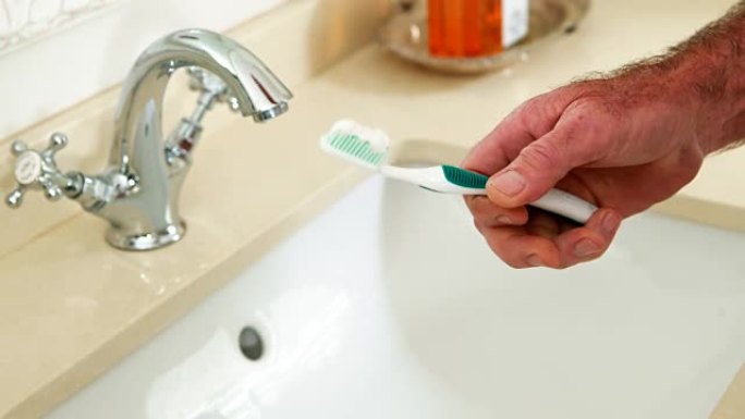 高级男子将牙膏放在浴室的牙刷上
