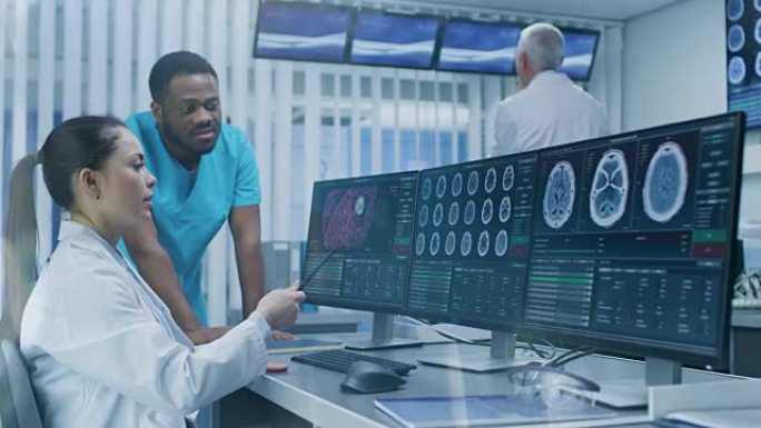 医学科学家和外科医生在实验室的个人计算机上讨论CT脑部扫描图像。神经学研究中心的神经学家/神经科学家