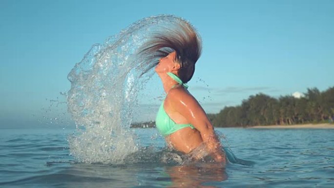 慢动作: 穿着绿松石比基尼的女孩将头发向后鞭打并喷水。