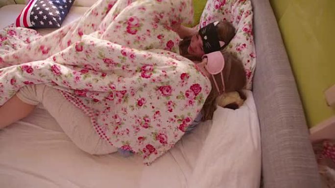 青春期女孩躲在床罩下戴着睡眠面具