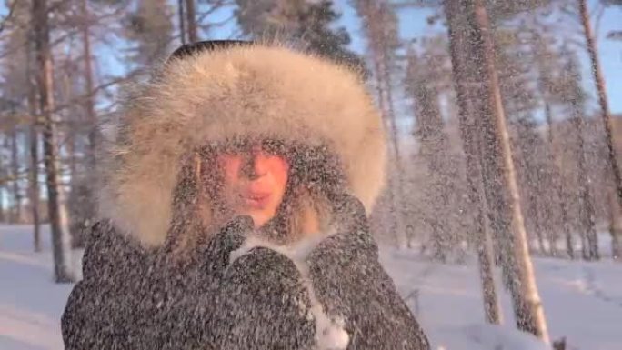 慢动作年轻女子在冬天将闪闪发光的白色雪花吹入相机