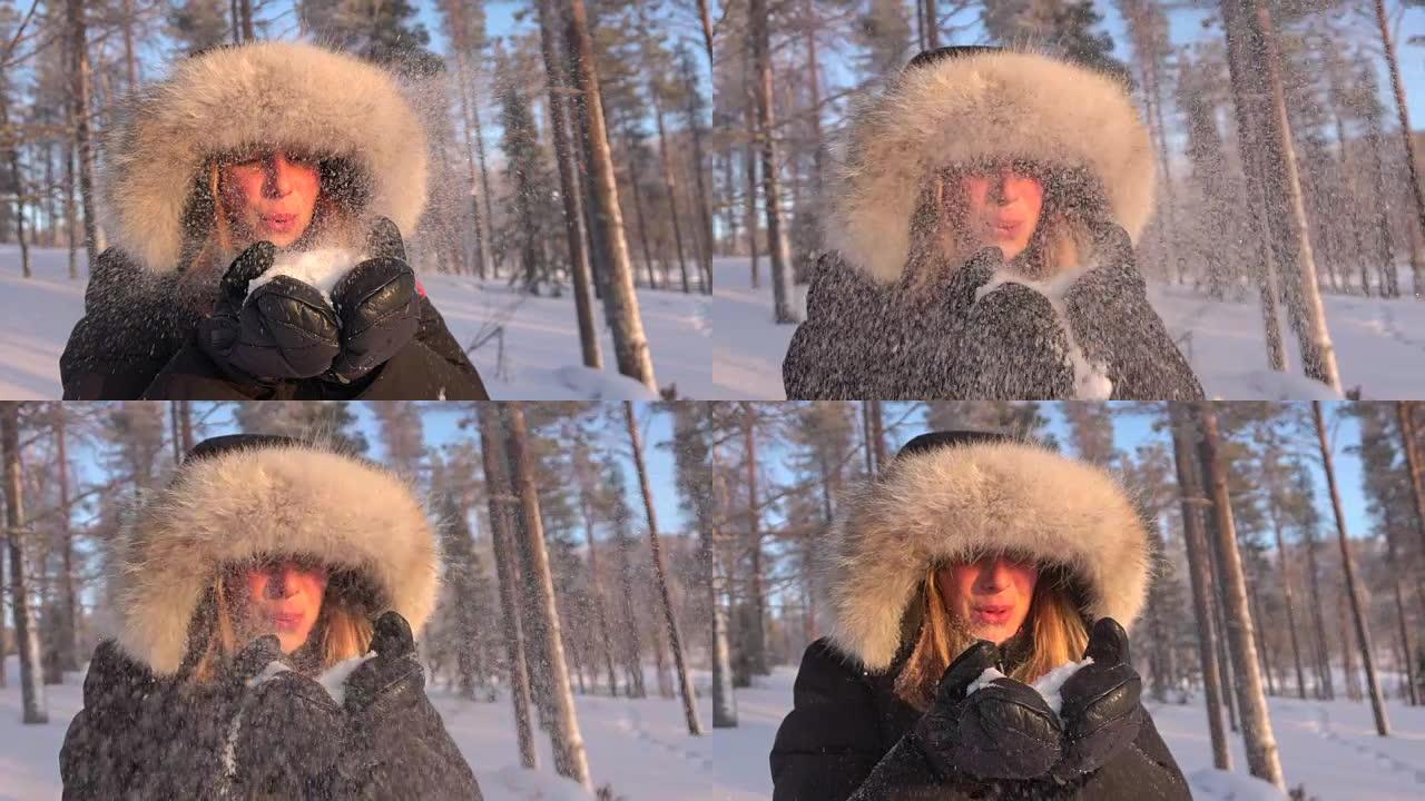慢动作年轻女子在冬天将闪闪发光的白色雪花吹入相机