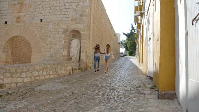 两个女性朋友走过古老的伊比沙岛，后视图