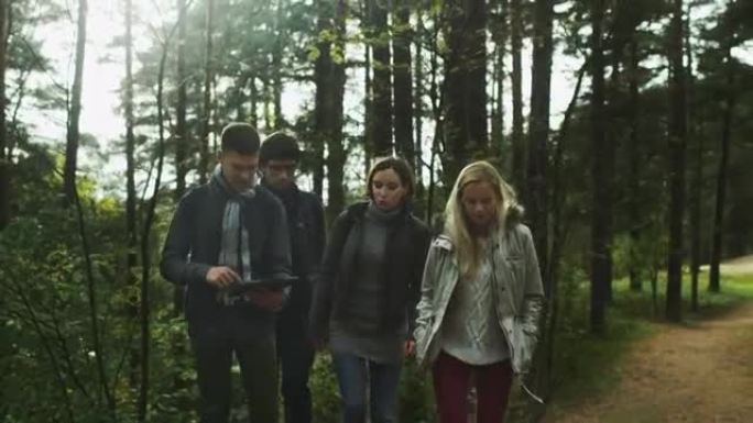 一群朋友正在森林中检查平板电脑，并继续前进。