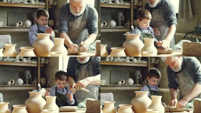 经验丰富的男陶工正在混合和揉捏粘土，而他可爱的小孙子正在车间帮助他。陶器、家庭传统和童年观念。