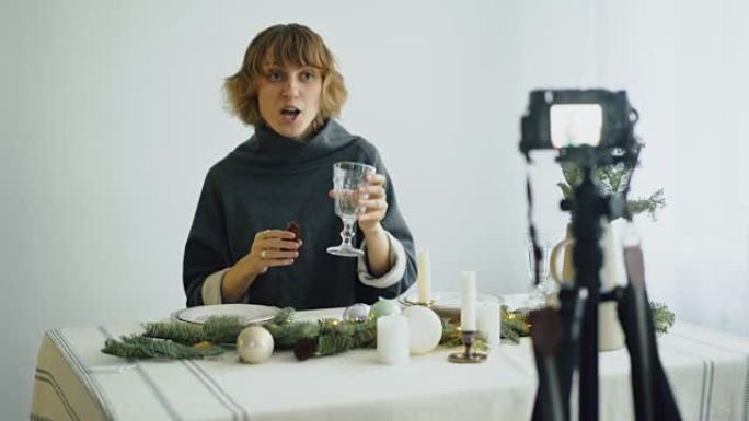 迷人开朗的女人坐在桌子旁录制视频博客关于相机上的食品装饰设计