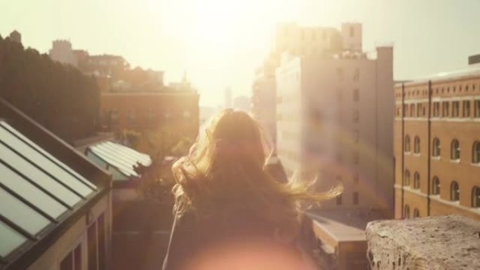 美丽的女人站在屋顶上，风拖着她长长的红头发。纽约市的城市景观，拥有巨大的摩天大楼和建筑。
