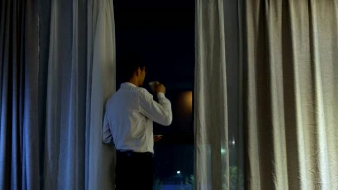 男人晚上站在窗边喝咖啡