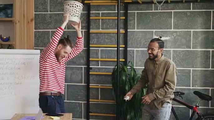 两个多种族的男人玩篮球游戏，在现代办公室的垃圾桶里扔纸